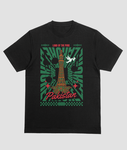 A black short-sleeve crewneck t-shirt featuring a graphic print of the Pakistan National Monument (miner e Pakistan Tower) in Lahore, with a white dove, green sunburst patterns, and red text reading 'Pakistan' and 'Land of the Pink'.